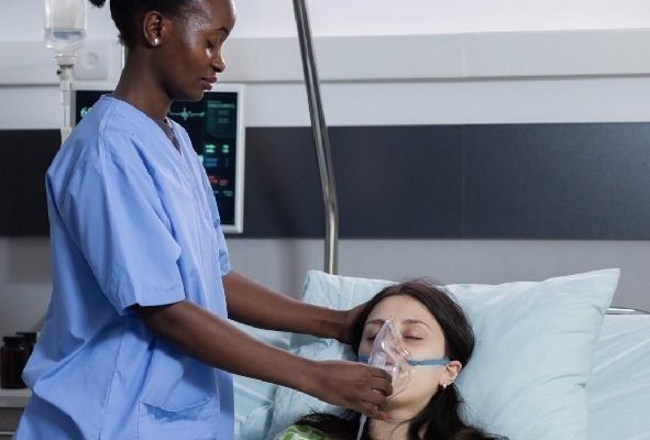 Médica de pie sosteniendo mascarilla de oxígeno de paciente en camilla