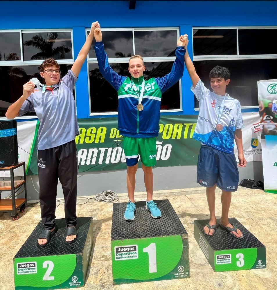 Tres jóvenes deportistas celebran con sus medallas en el podio de premiación de los Juegos Deportivos Institucionales.