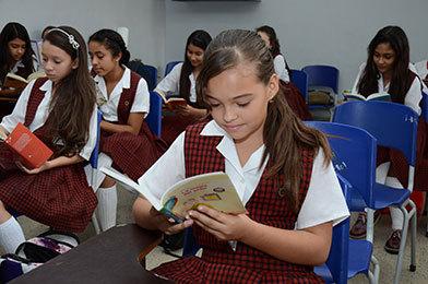 Estudiantes de bachillerato femenino sentadas cada una en su puesto leyendo un libro