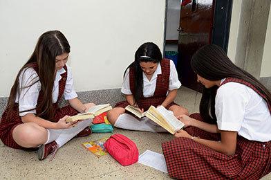 Tres estudiantes del bachillerato femenino sentadas en el piso, en la entrada del salón, cada una leyendo un libro
