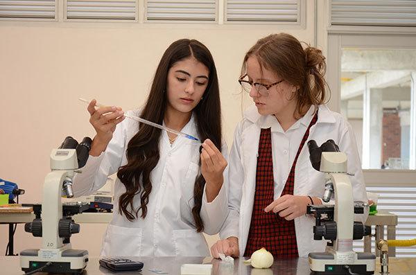 Dos estudiantes del bachillerato femenino en un laboratorio con un microscopio y una pipeta graduada