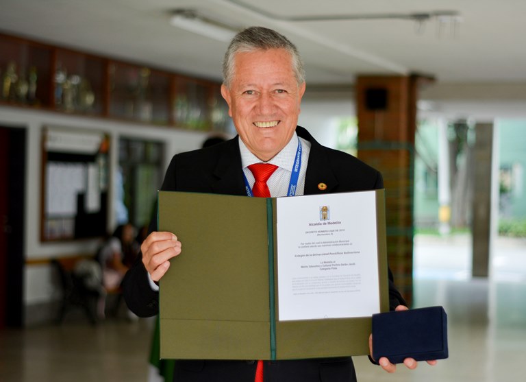  Reconocimiento al Mérito educativo al Mérito Educativo y Cultural Porfirio Barba Jacob, categoría plata siendo sostenido por el rector, Ómar Peña Muñoz.