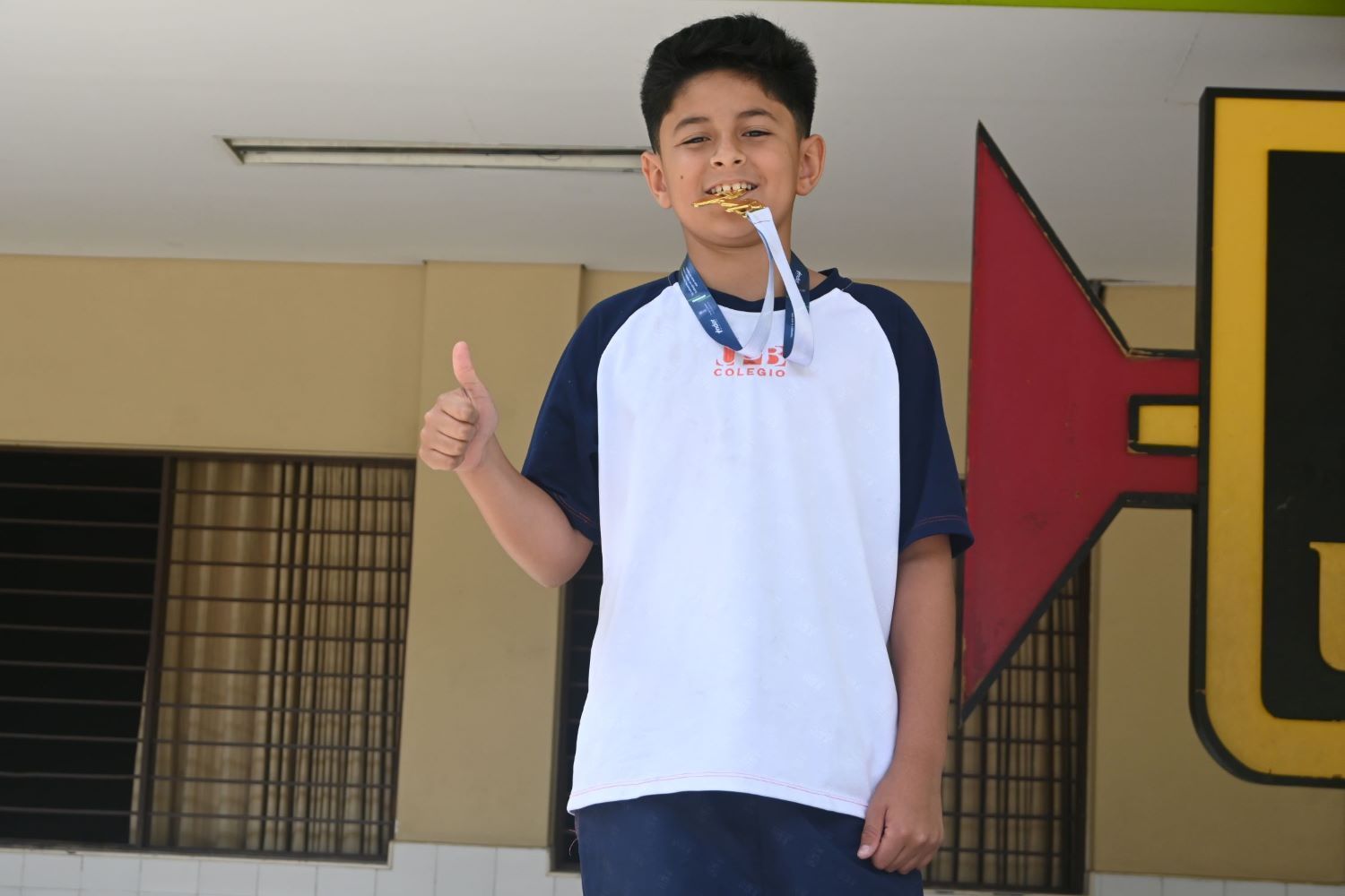 Niño con uniforme escolar celebra mostrando su medalla de oro.
