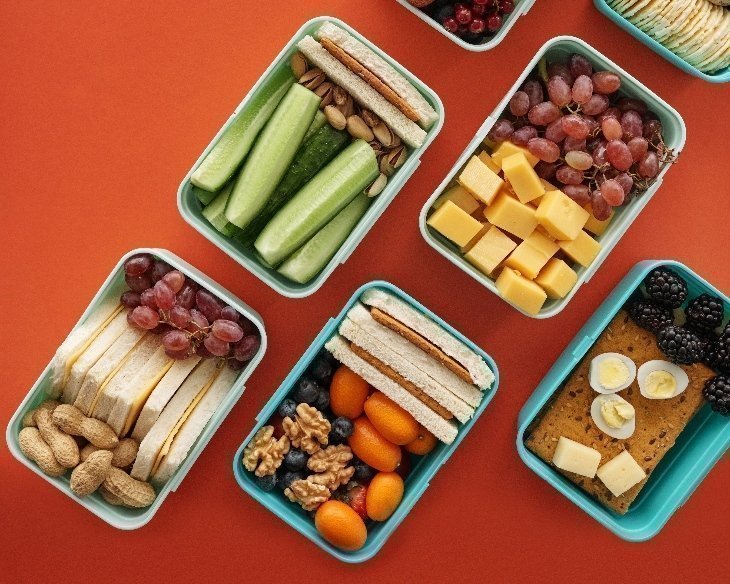 Vista aérea de diferentes recipientes que contienen alimentos saludables, sobre mesa color anaranjado