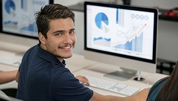 estudiante al frente de un computador, mira a la cámara sonriente