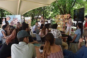 las personas se encuentran visualizando los libros que la editorial está ofreciendo, al fondo se encuentran unos banderines característicos de un festival