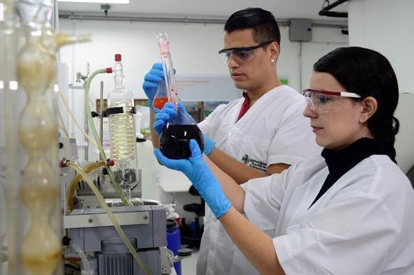 personas en el laboratorio manipulando unos tubos de ensayos con sustancias químicas. las personas usan bata, gafas transparentes y guantes