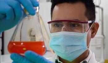 Persona que usa gafas de seguridad transparentes y un tapabocas en un laboratorio. Sosteniendo un tubo de ensayo con una sustancia química