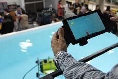 manos que sostienen el dispositivo que controla el robot que se encuentra sumergido en el agua
