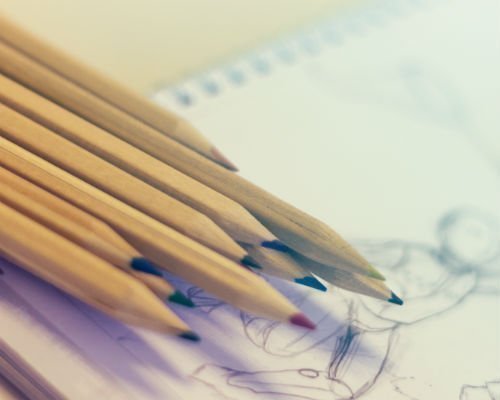 lápices de colores sobre un cuaderno que tiene el boceto de un dibujo
