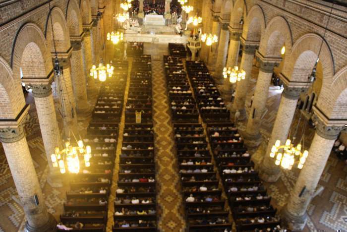 Imagen del interior de la Catedral con gente en las bancas tomada desde arriba. Se destacan los arcos de la construcción.