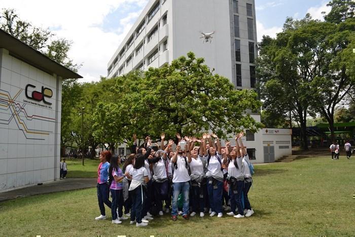 Grupo de estudiantes de colegio en las zonas verdes de la Universidad mirando hacia un dron