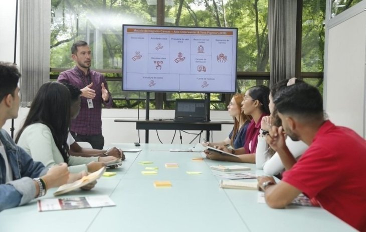 Grupo de personas en una sala de reuniones, observando una presentación en pantalla.