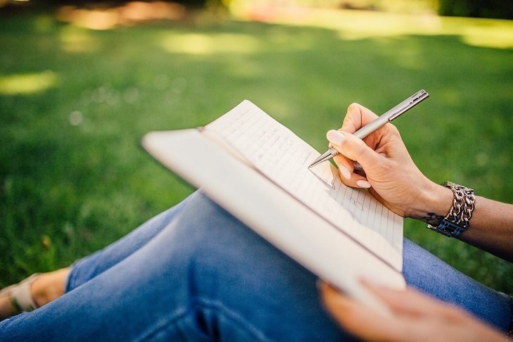 Mujer sentada en un césped escribiendo