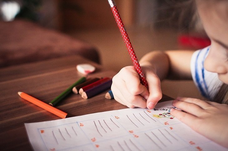 Sobre un escritorio se encuentra un niño, con unos colores, pintando una imagen en un cuaderno.