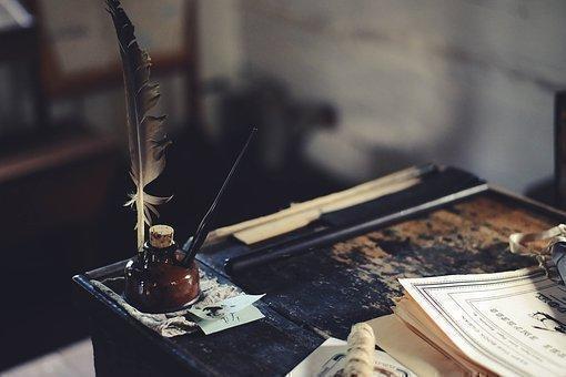 Sobre un escritorio viejo se encuentran unas hojas, un tintero y una pluma