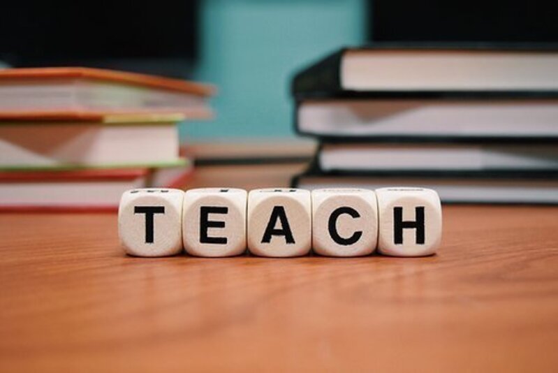 Sobre una superficie se encentran unos libros y un letrero que forma la palabra "teach" (enseñar).