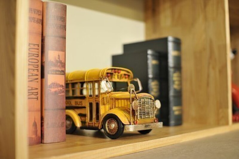 En una biblioteca se encuentran unos libros y en la mitad de ellos está un bus amarillo de colección.de 