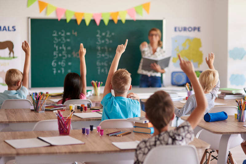 Salón de clases con estudiantes levantando la mano para participar