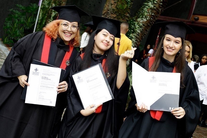 Tres estudiantes mujeres con diploma y toga de graduación