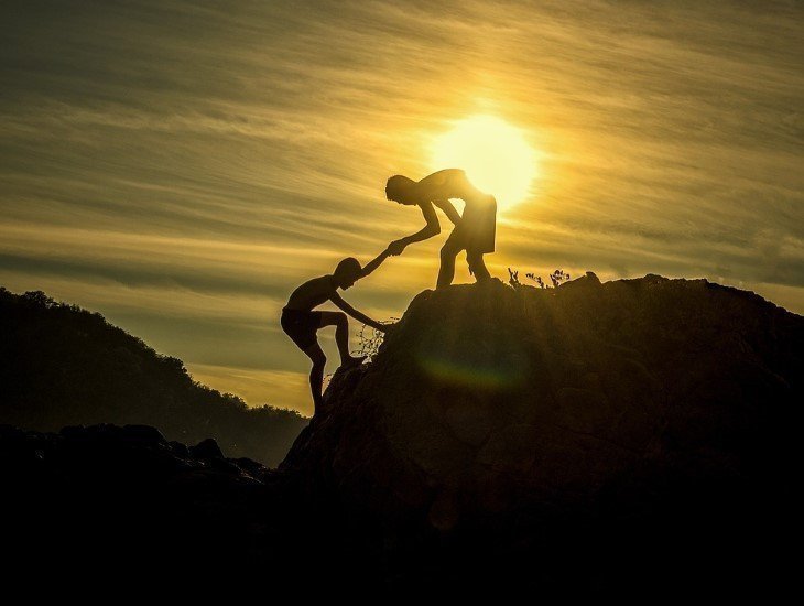 Persona ayudando a subir a otra en una montaña, bajo el atardecer