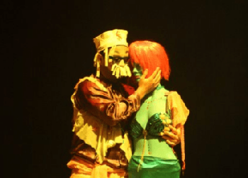 Dos actores con vestuario colorido se abrazan 