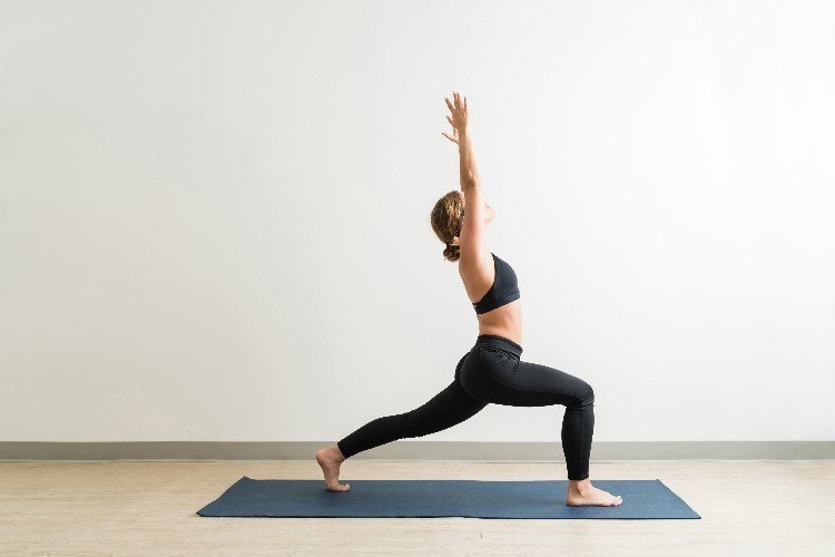Mujer de pie en una manta realizando la postura del guerrero de yoga, en su variante número uno